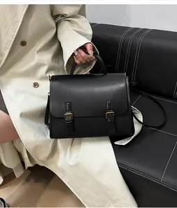 Detail of a vintage black messenger bag with gold metal buckles on a leather sofa
