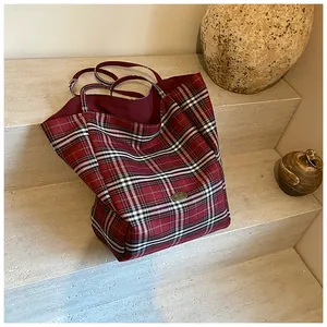 Macro shot of large red plaid tote bag with handmade metal logo on stone stairs