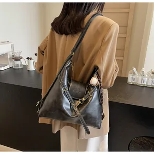 Detalle del bolso tote de cuero negro con correa ancha y colgante de béisbol en vista lateral