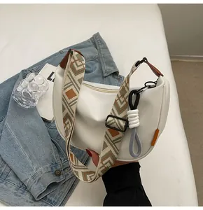 Detailansicht weiße Halbmond-Tasche mit gemustertem breitem Gurt auf Jeansjacke
