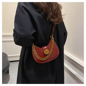 Detail of burgundy crescent crossbody bag with glossy leather and gold chain strap