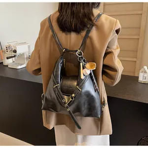 Detalle de una mochila grande de cuero negro con un colgante de béisbol en un café