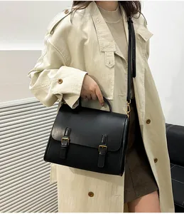 Classic black vintage messenger bag shown worn with a beige trench coat for a stylish look