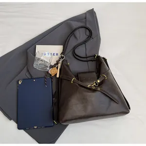 Detalle de bolso tote de cuero marrón oscuro con herrajes dorados sobre chaqueta