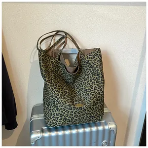 Detail of leopard print tote bag with metal 'Handmade' tag on a silver suitcase