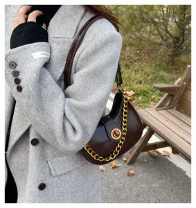 Detail of dark brown crescent shoulder bag with golden rotary buckle and chain ornament