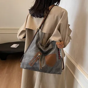 Retro grey crossbody tote bag with brown straps and plush bear charm worn by a model