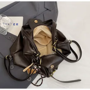 Detalle de bolso tote de cuero marrón oscuro con dijes de béisbol y cierre magnético