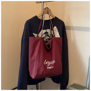 Detail of burgundy canvas tote bag with beyou print and plaid lining strap