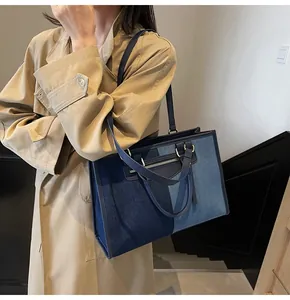 Detalle de bolso tote de mezclilla bicolor con borlas sobre una gabardina beige