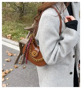 Close-up of brown crescent shoulder bag with golden hardware and woven tassel detail