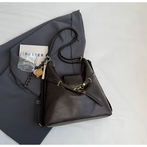 Vista detallada del bolso tote de cuero marrón oscuro con hebilla y colgante de béisbol
