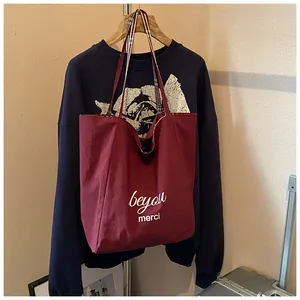 Close-up of deep red tote bag with beyou merci print hanging on a blue sweatshirt