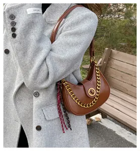 Detail of a brown leather saddle bag with gold chain and woven charm on a grey coat