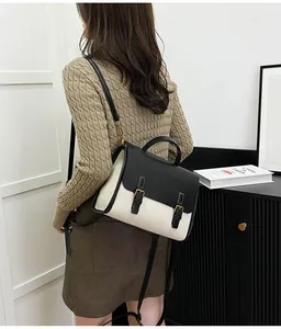 Model wearing a dual-tone canvas backpack with black leather trim in a minimalist room