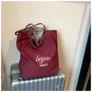 Detail of red tote bag with beyou merci print hanging on a silver suitcase handle