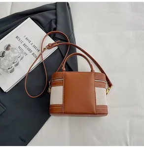Dettaglio delle cuciture in pelle marrone e tela beige su una piccola borsa a scatola