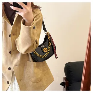 Detail of black crescent shoulder bag featuring gold chain and red tassel charm detail