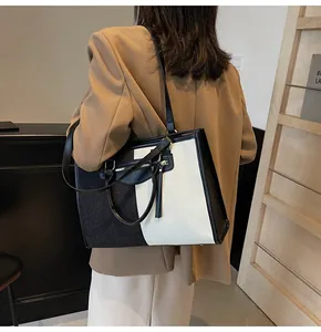 Detalle de un bolso tote grande en contraste blanco y negro con asas dobles y bolsillo de metal