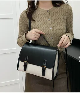 Detail of a beige textured messenger bag with black leather flap and gold metal buckles