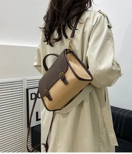 Side view of a vintage beige canvas and brown leather messenger bag worn on a beige coat
