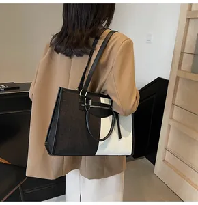 Bolso tote de lona bicolor con ribete de cuero lucido por modelo con traje beige
