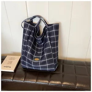 Detail of blue and white checkered canvas tote bag with a golden metal logo plate