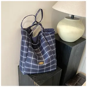 Close-up of handmade metal logo on a blue checkered canvas tote bag with shoulder straps
