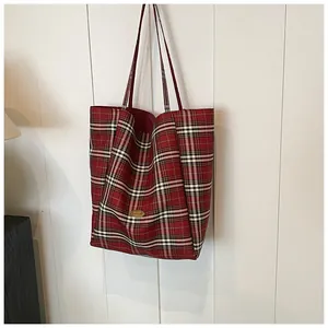 Detail of red plaid tote bag featuring a golden handmade metal plaque and slim shoulder strap