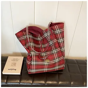 Detail of red plaid tote bag with handmade gold metal logo on a leather seat