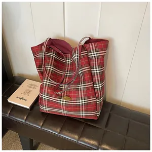Macro detail of red tartan plaid pattern and golden brand logo on a large tote bag