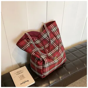 Close-up of red tartan tote bag with metal nameplate on a leather bench