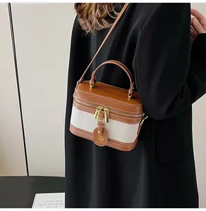 Dettaglio di una borsa a tracolla in pelle marrone e tela beige con eleganti cuciture bianche