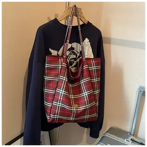 Close-up of red plaid canvas tote bag with 'Handmade' metal logo and red interior lining