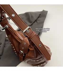 Détail de la bandoulière en cuir réglable avec œillets argentés et clous sur sac brun