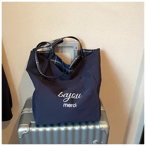 Macro detail of navy nylon tote bag showing white logo print and blue plaid inner lining