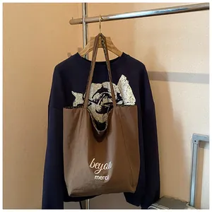 Detailed close-up of brown tote bag with merci print and leopard strap on a gold hanger