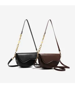 Detail view of smooth leather saddle bags in black and dark brown with gold chain straps