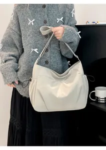 Close-up of cream nylon crossbody bag with side drawstrings worn on the shoulder