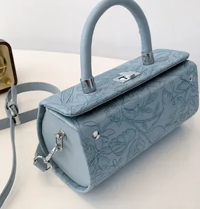 Detail view of light blue embossed leather cylinder bag with floral texture and silver lock