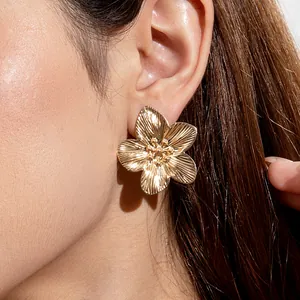 Detail of golden five-petal flower earring with textured petals on model's ear