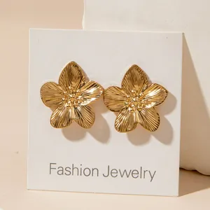 Detailed view of gold flower earrings with pleated texture and pearl centers on display card