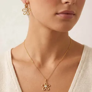 Gros plan d'un ensemble bijoux fleur en acier doré porté au cou et aux oreilles