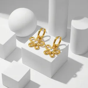 Détail de créoles fleurs dorées avec zircone transparent dans un décor minimaliste