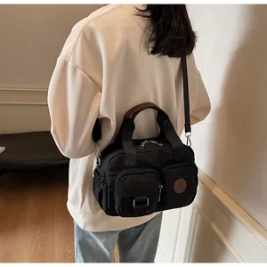 Detail of black multi-pocket canvas crossbody bag with brown leather handles and dual zippers