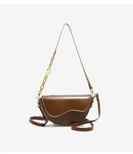 Detailed view of brown saddle bag with asymmetrical flap and gold chain strap