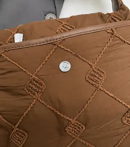 Close-up of brown quilted fabric with rhombic embroidery and silver metallic logo detail