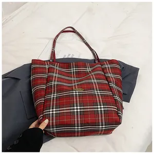 Detail of red plaid canvas tote bag with handmade metal emblem on stylish blazer background
