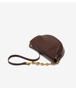 Detailed close-up of dark brown leather saddle bag with gold chain strap and wave flap edge