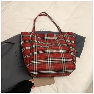 Detail of red plaid tote bag featuring a metal Handmade tag and sturdy canvas handles